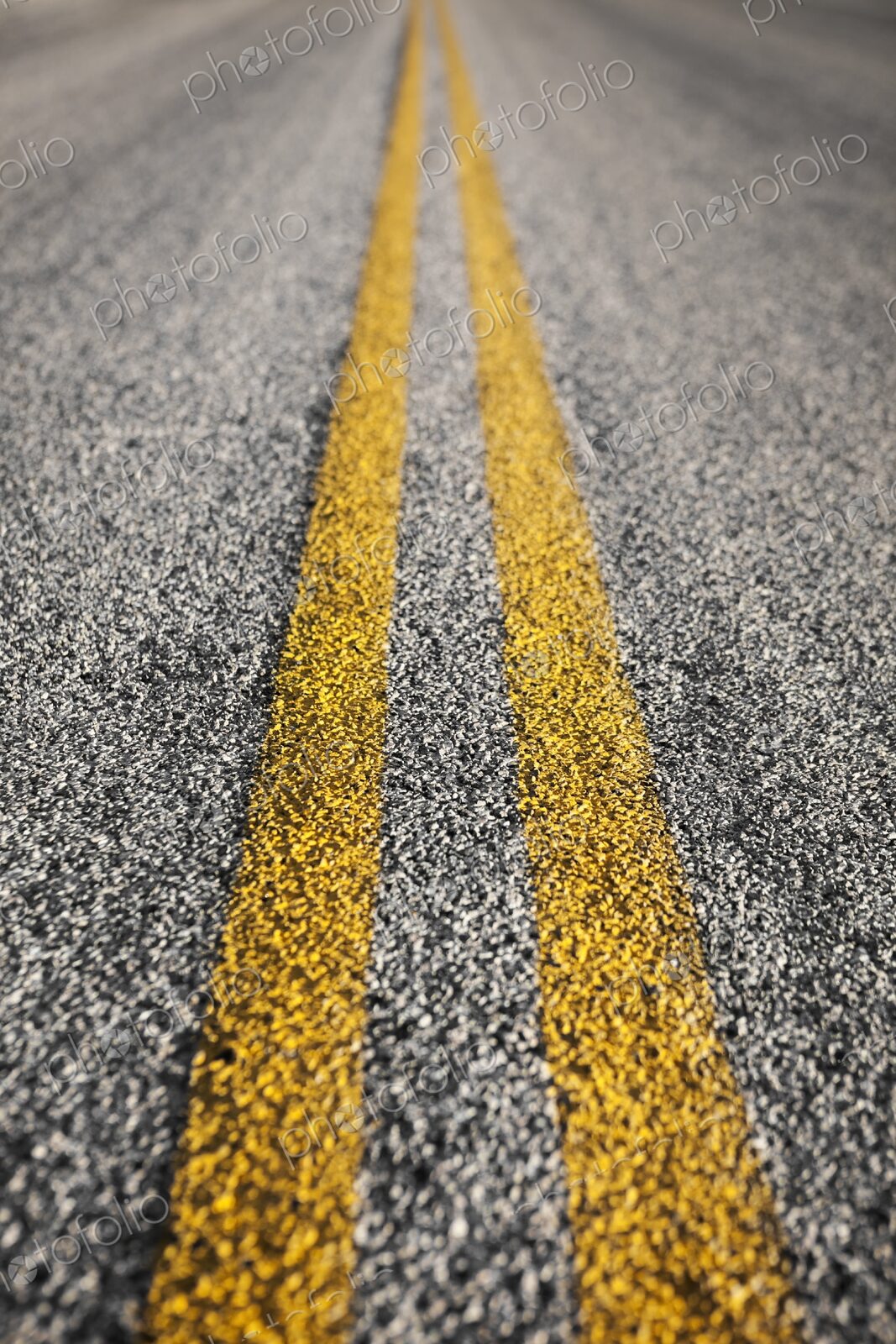Detailed close-up of yellow double lines painted on an asphalt road, symbolizing…