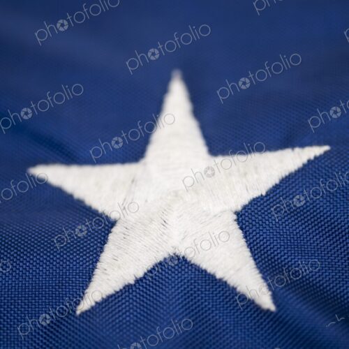 Detailed macro image of a single embroidered white star on the blue field of the…