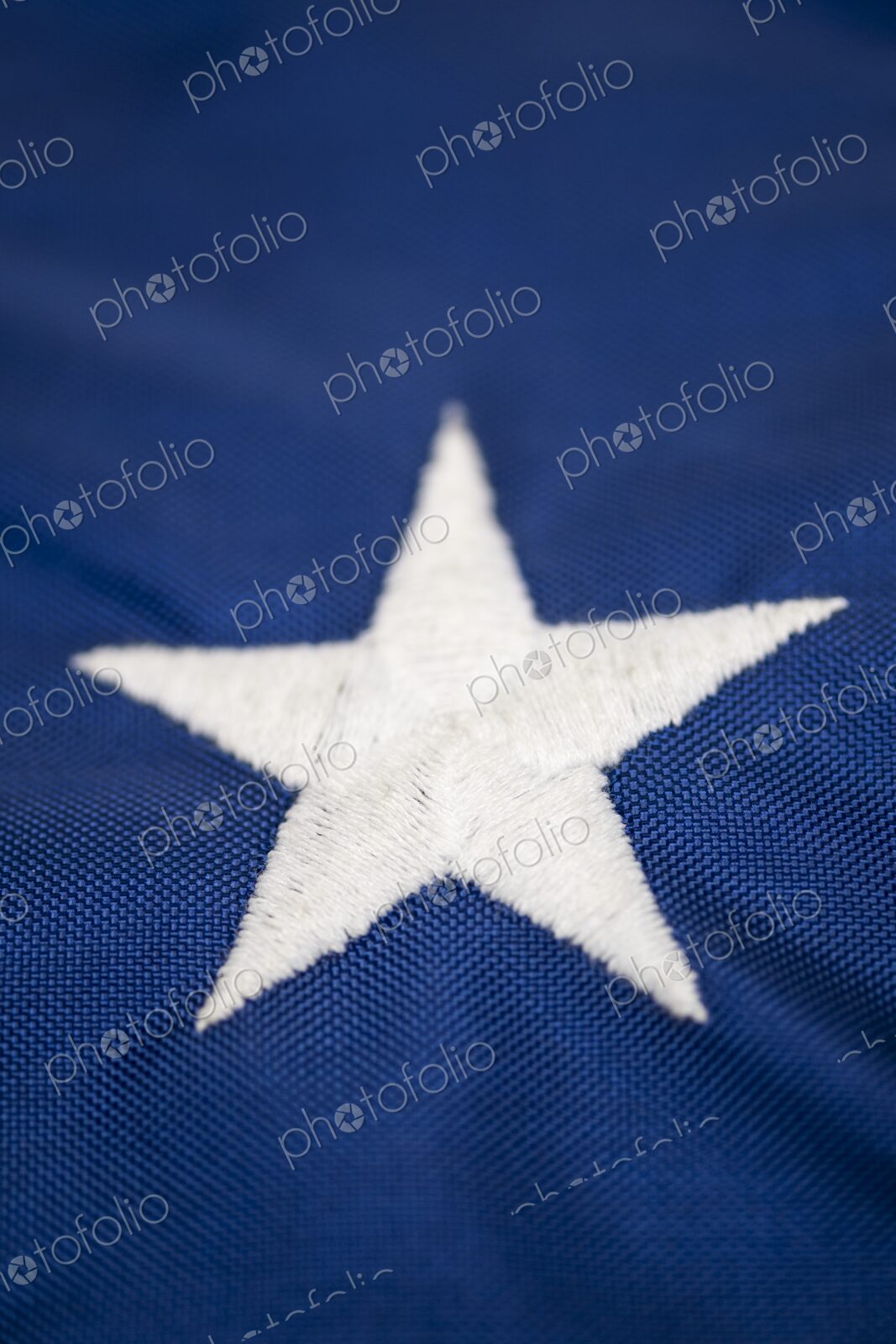 Detailed macro image of a single embroidered white star on the blue field of the…