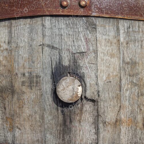 Detailed view of a weathered wooden barrel with cork, secured with rusted iron bands,…