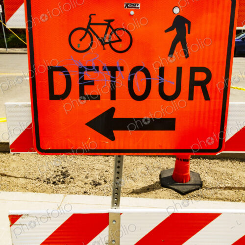Detour sign on a pavement for pedestrians and cyclists, and a red and white barrier.