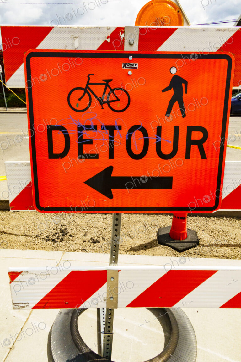 Detour sign on a pavement for pedestrians and cyclists, and a red and white barrier.