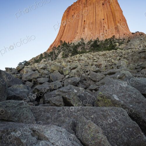 Devil's Tower glows orange in the evening light, rising above rocky slopes and pine… Devil's Tower glows orange in the evening light, rising above rocky slopes and pine…