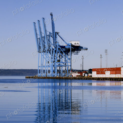 Dockside cranes silhouetted against the sky at dusk, shadows on the water, at the port…