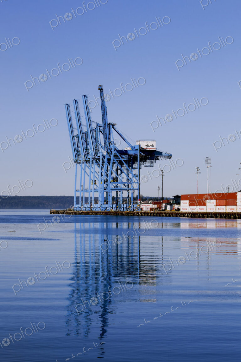 Dockside cranes silhouetted against the sky at dusk, shadows on the water, at the port…