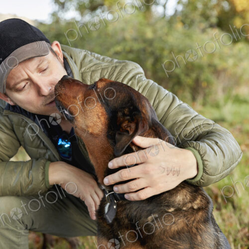 Dog walker bending down to stroke a dog nuzzling his face. Dog walker bending down to stroke a dog nuzzling his face.