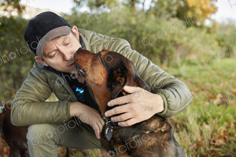 Dog walker bending down to stroke a dog nuzzling his face.