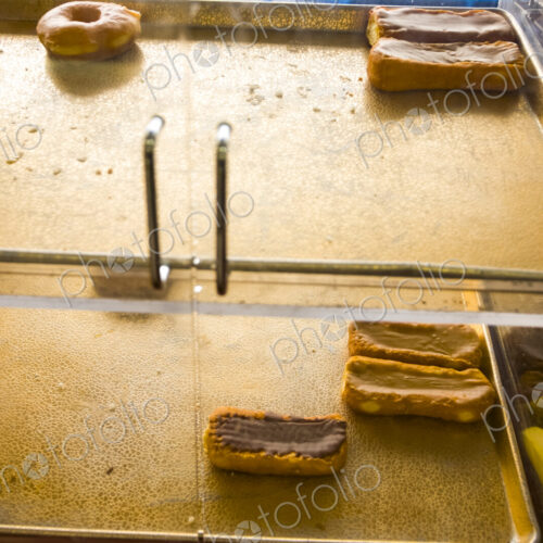 Donuts and cakes with chocolate icing on a tray in a shop window, a few left.