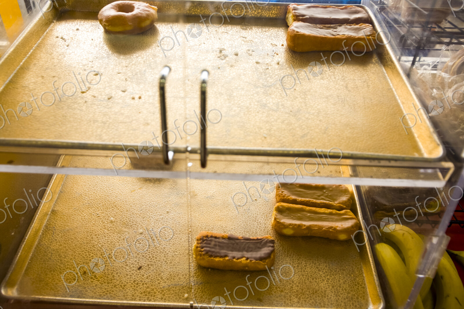 Donuts and cakes with chocolate icing on a tray in a shop window, a few left.