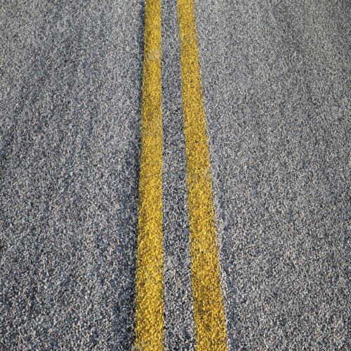 Double yellow lines painted on an asphalt road, symbolizing travel, direction, and… Double yellow lines painted on an asphalt road, symbolizing travel, direction, and…
