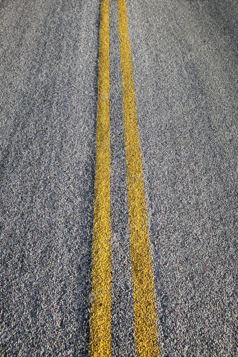 Double yellow lines painted on an asphalt road, symbolizing travel, direction, and…