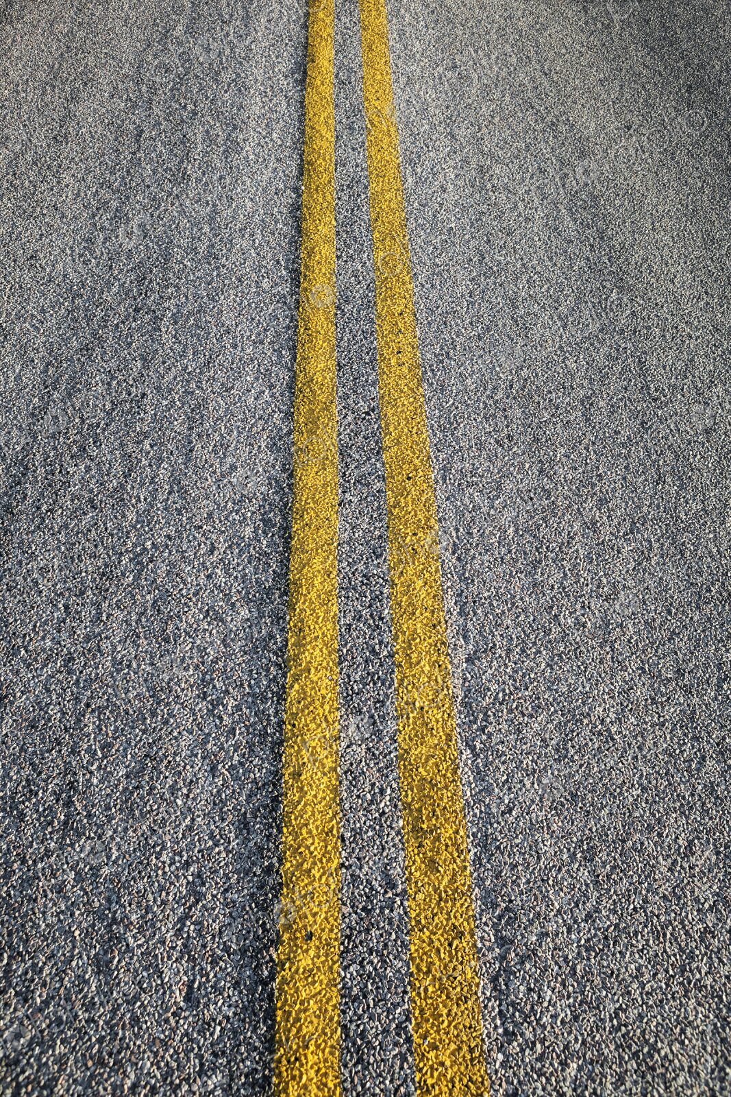 Double yellow lines painted on an asphalt road, symbolizing travel, direction, and…