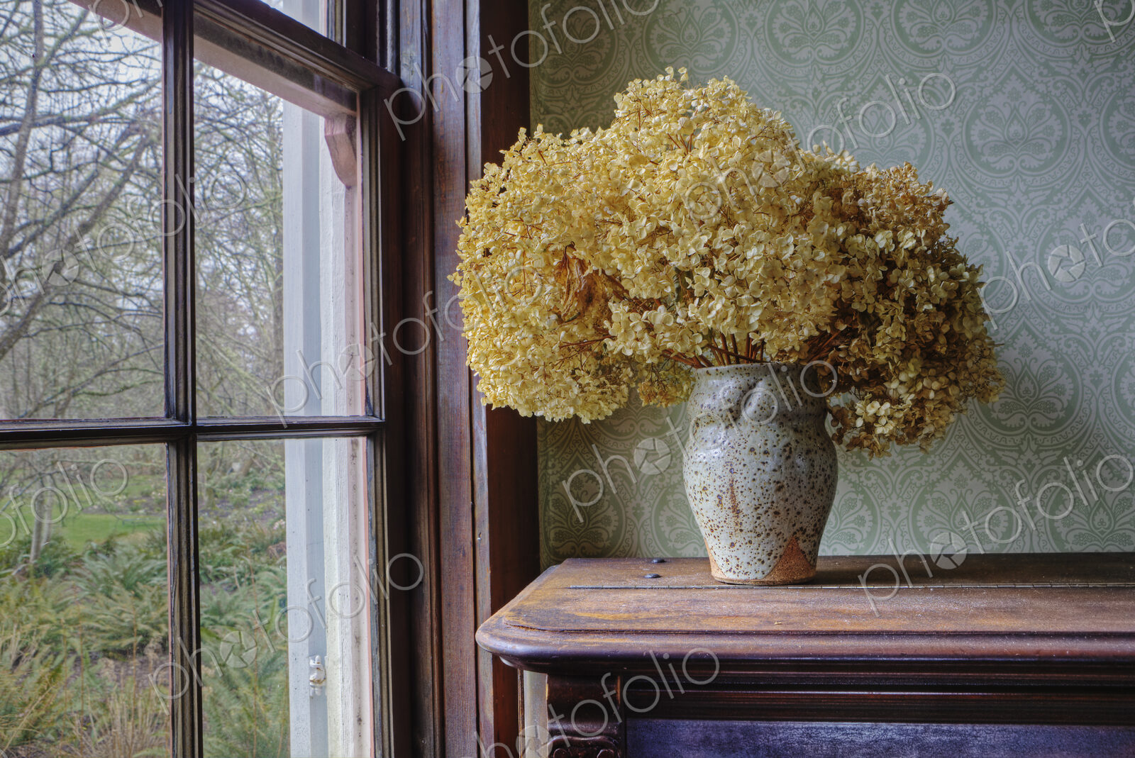 Dried flowers in a vase on a shelf by a window.