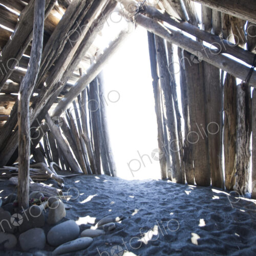 Driftwood hut interior on sand.