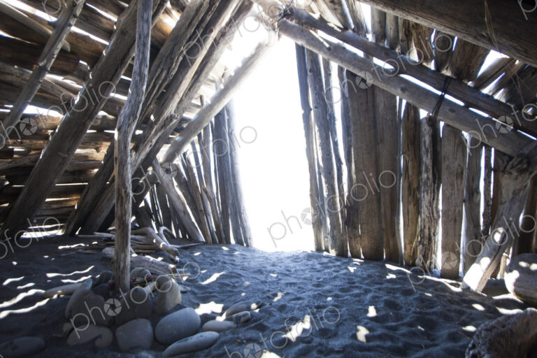 Driftwood hut interior on sand.