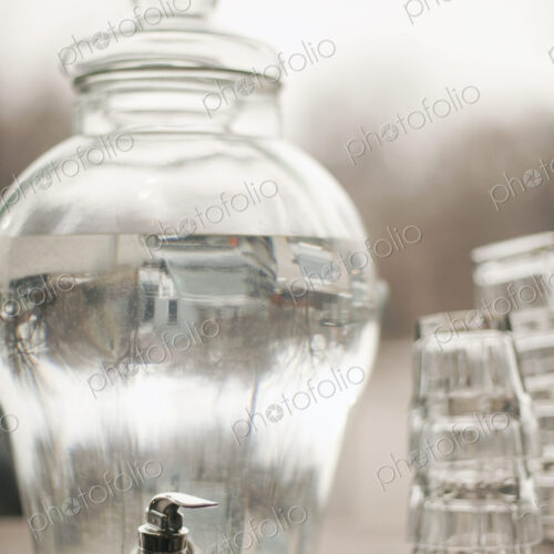Drinking water in a large clear glass container. A stack of glasses. Pure chilled water. Drinking water in a large clear glass container. A stack of glasses. Pure chilled water.
