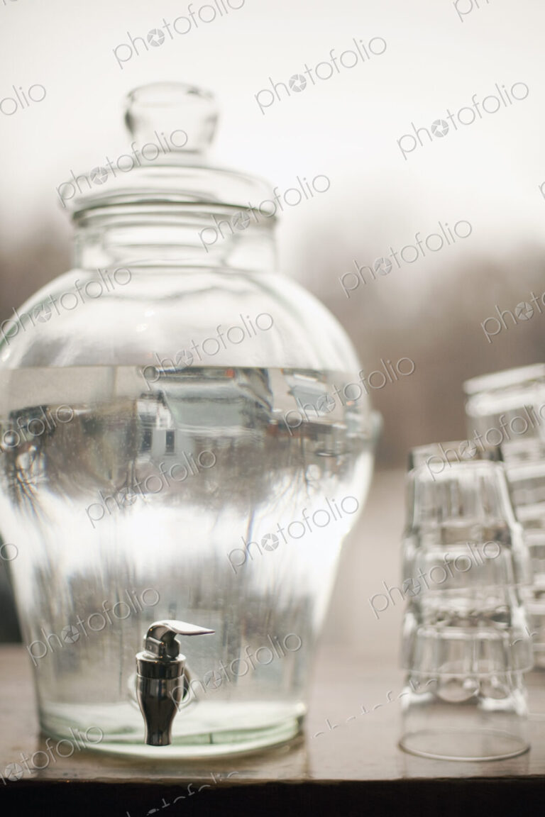 Drinking water in a large clear glass container. A stack of glasses. Pure chilled water.