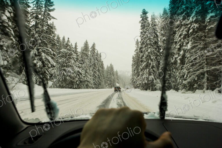 Driver's view through the windscreen of a snowy road and cars driving, a driver's hand…