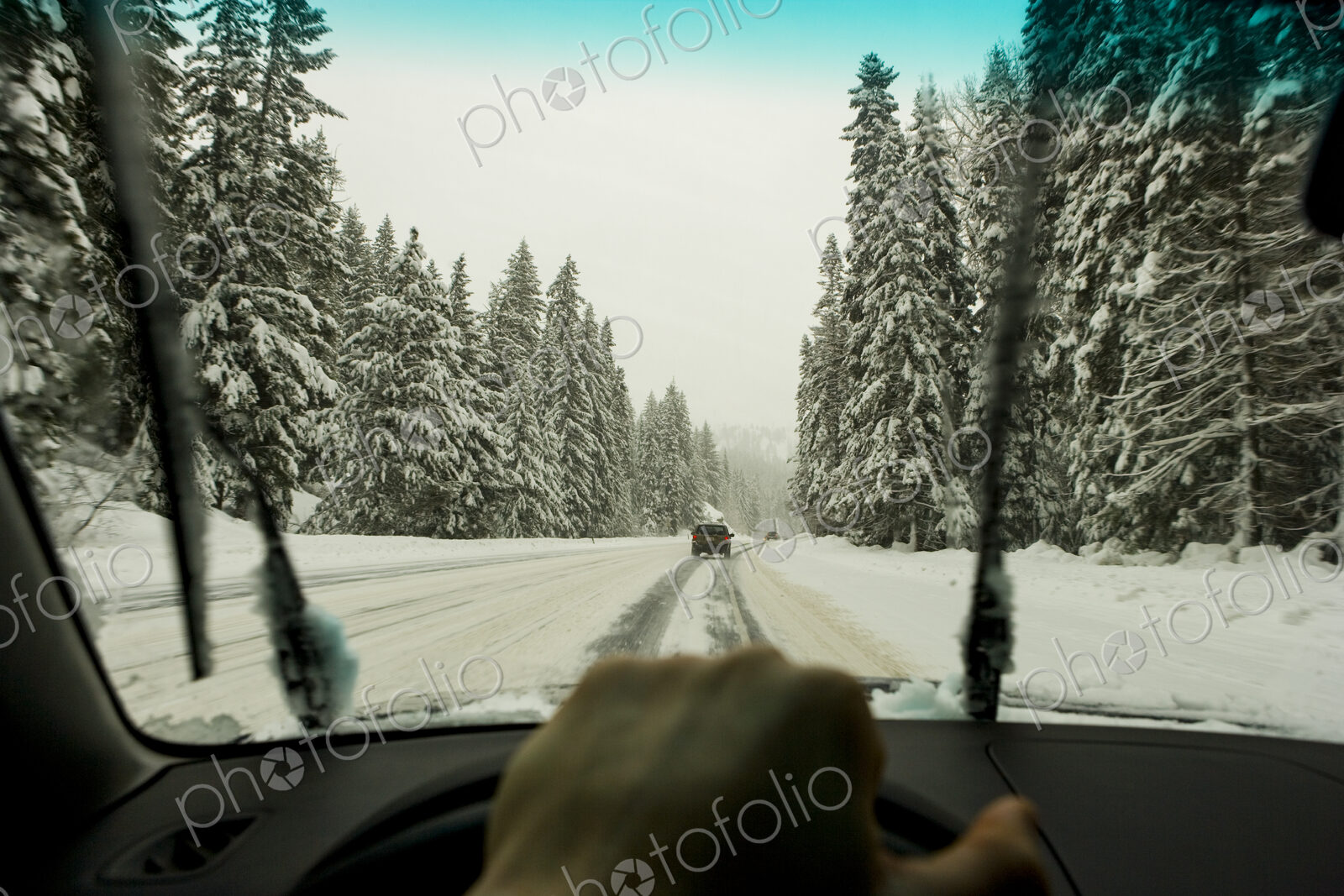 Driver’s view through the windscreen of a snowy road and cars driving, a driver’s hand…
