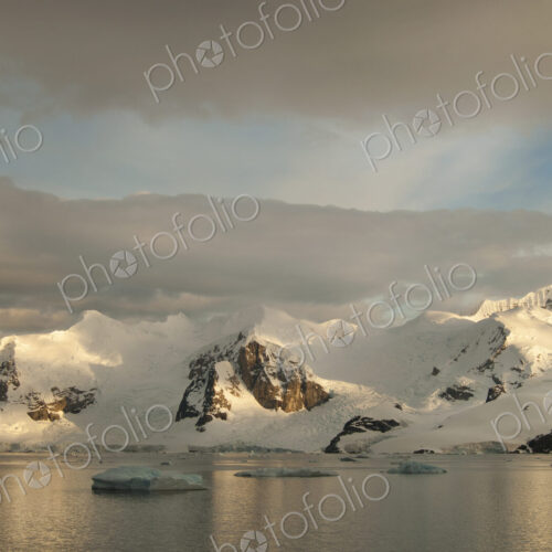 Dusk and flat calm water off the shore of a mountain landscape in Antarctica. Dusk and flat calm water off the shore of a mountain landscape in Antarctica.