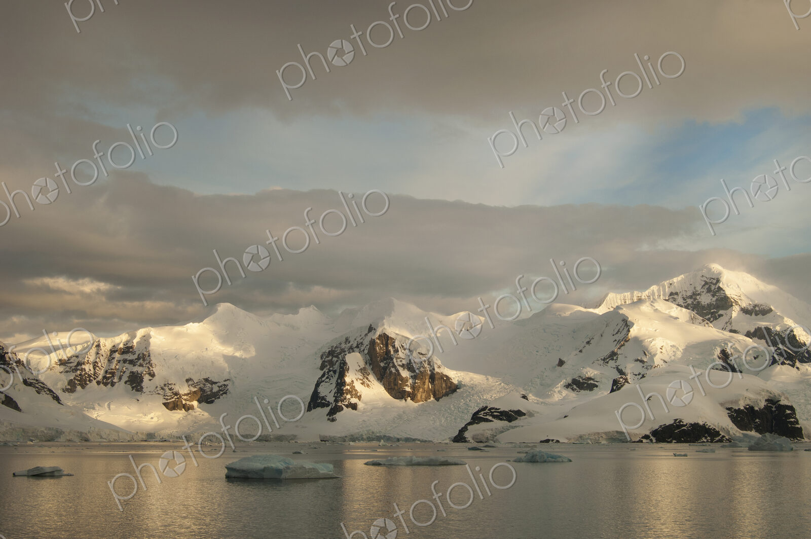 Dusk and flat calm water off the shore of a mountain landscape in Antarctica.