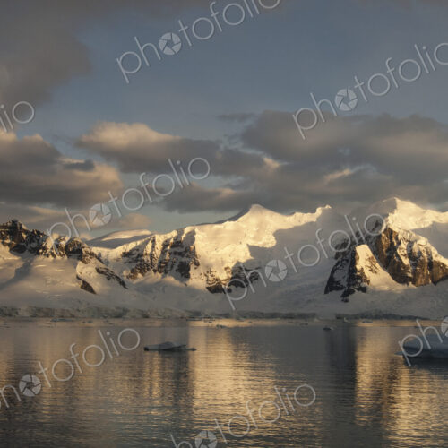 Dusk and flat calm water off the shore of a mountain landscape in Antarctica. Dusk and flat calm water off the shore of a mountain landscape in Antarctica.