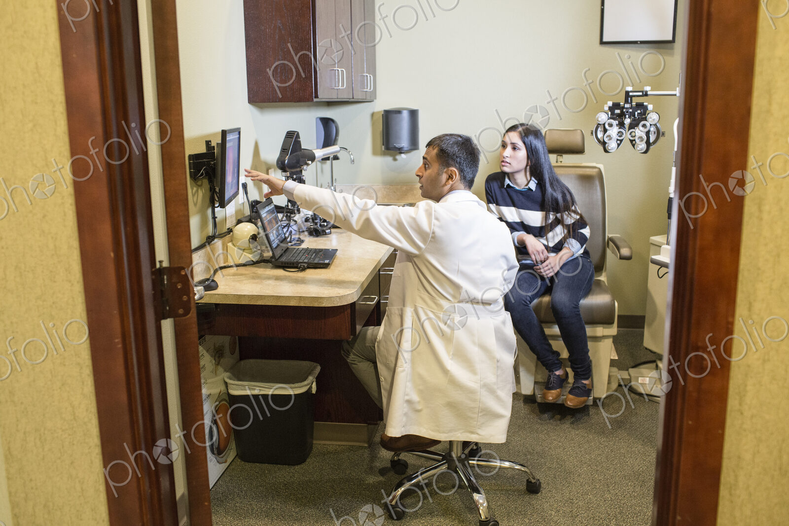 East Indian male ophthalmologist working with a female patient in his examination office.