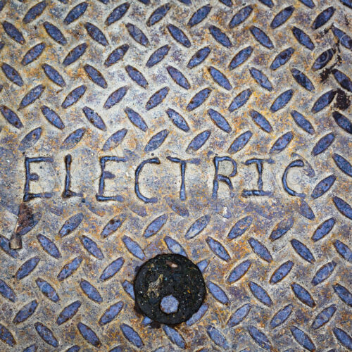 Electric man hole cover close up, a metal surface.