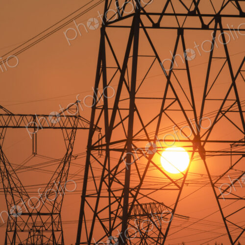 Electricity pylon and power lines with sun behind.