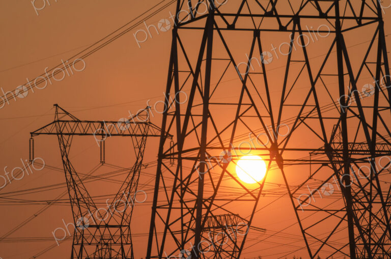 Electricity pylon and power lines with sun behind.