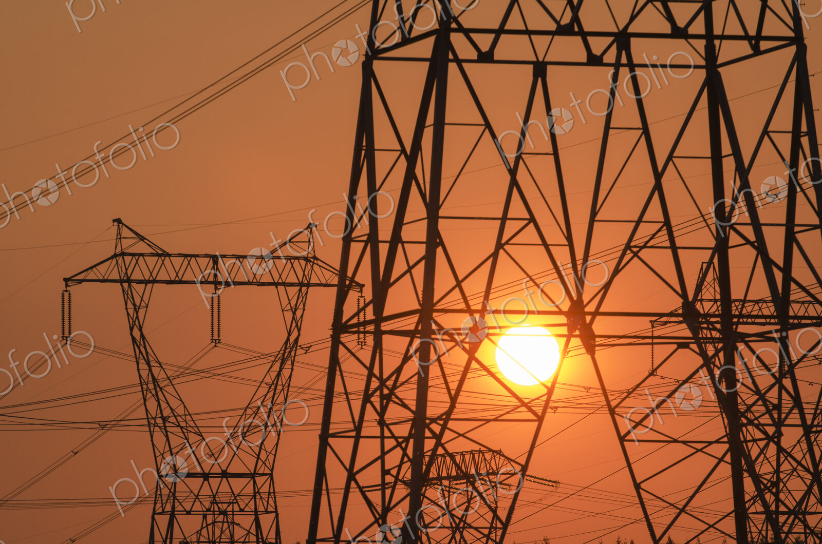 Electricity pylon and power lines with sun behind.