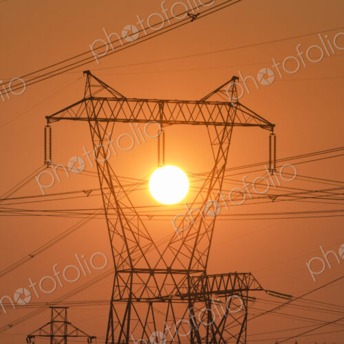 Electricity pylon and power lines with sun behind.