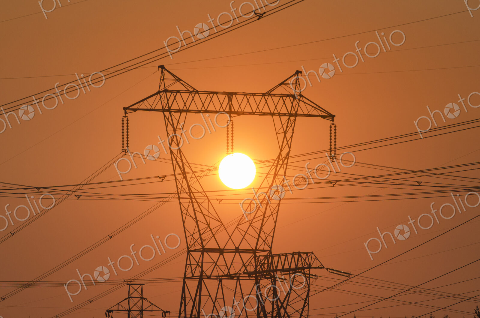 Electricity pylon and power lines with sun behind.