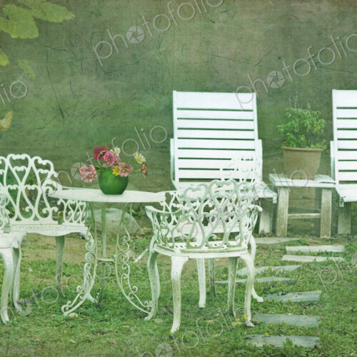 Elegant white painted garden chairs and table set out garden.