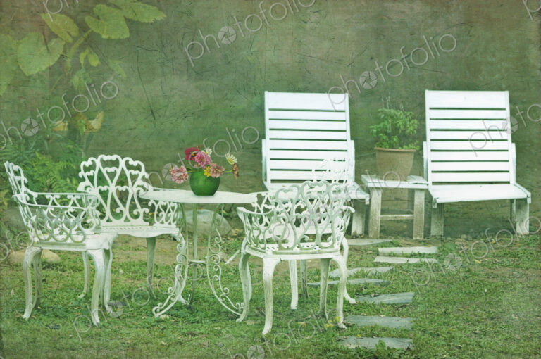 Elegant white painted garden chairs and table set out garden.