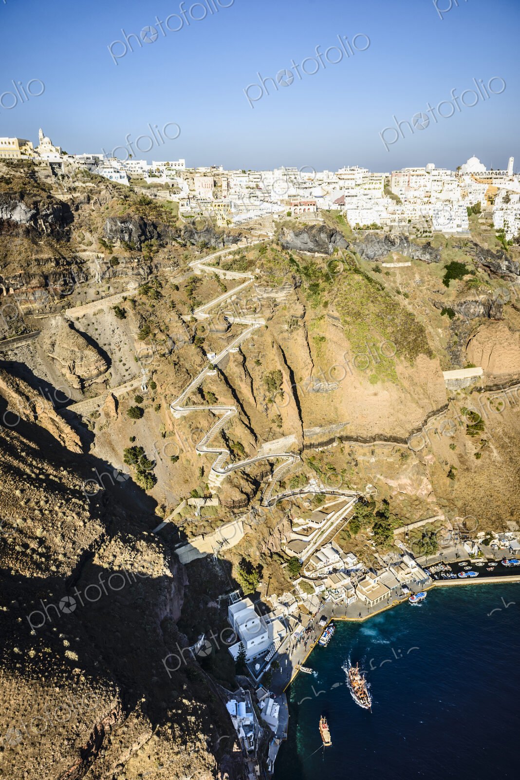 Elevated view of a steep cliff, hilltop town and a harbour on the water with a zigzag…