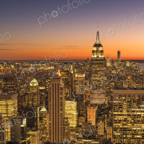 Empire state building rising above Manhattan skyline at sunrise or sunset.