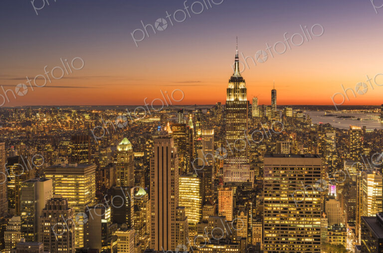 Empire state building rising above Manhattan skyline at sunrise or sunset.