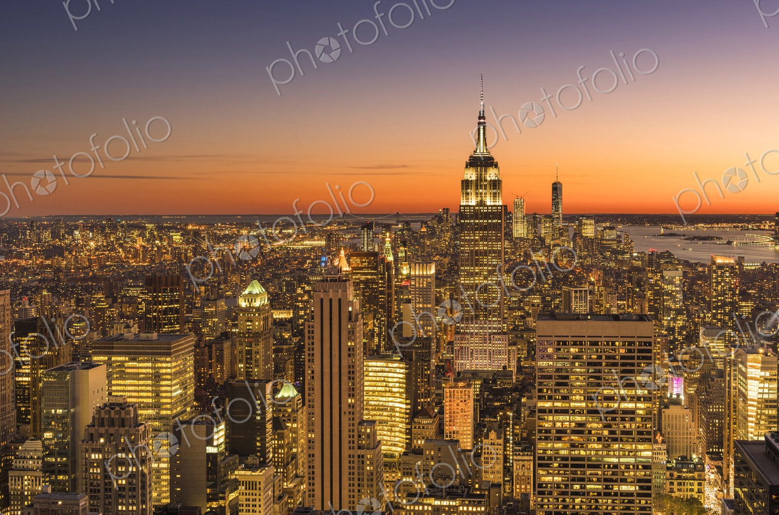 Empire state building rising above Manhattan skyline at sunrise or sunset.