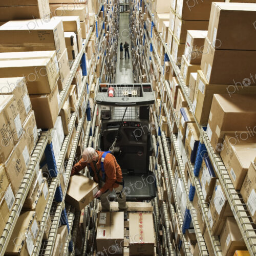 Employee picking a box using a motorised cherry picker platform in a distribution… Employee picking a box using a motorised cherry picker platform in a distribution…
