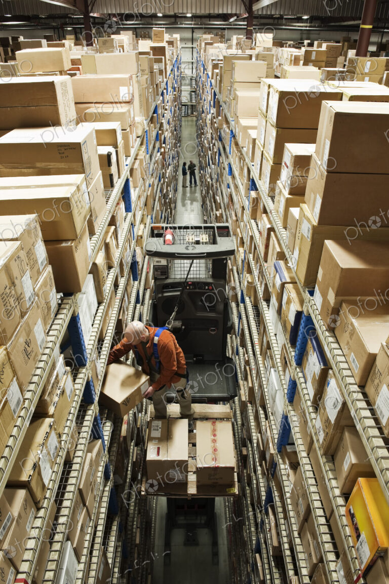 Employee picking a box using a motorised cherry picker platform in a distribution…