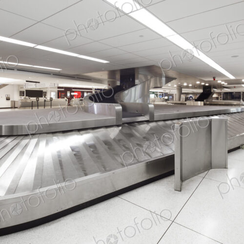 Empty airport luggage claim area, carousels and information screens.
