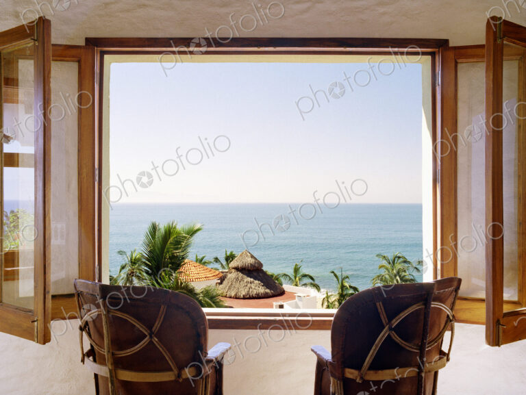 Empty chairs facing open window overlooking ocean
