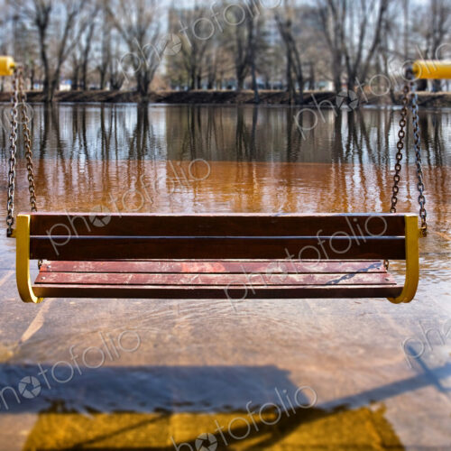 Empty hanging bench swing surrounded by hard frozen ice, riverbank