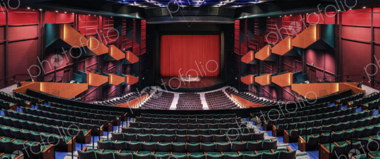 Empty theatre auditorium, stage with a red curtain, boxes and modern design.