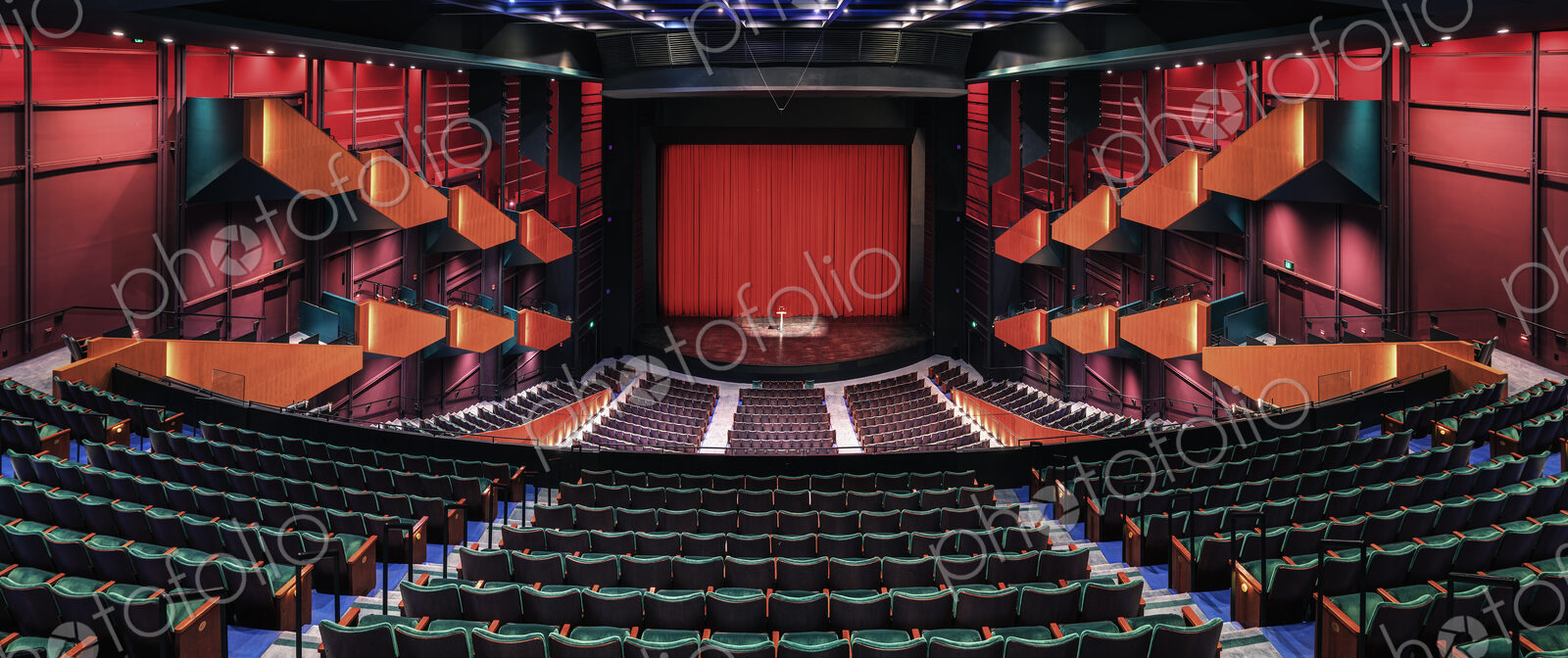 Empty theatre auditorium, stage with a red curtain, boxes and modern design.