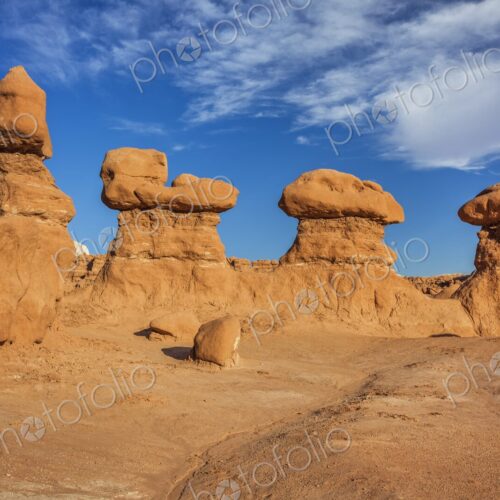 Eroded sandstone hoodoo rock formations under a bright blue sky with scattered clouds…