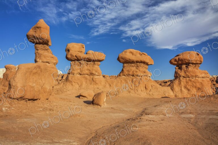 Eroded sandstone hoodoo rock formations under a bright blue sky with scattered clouds…