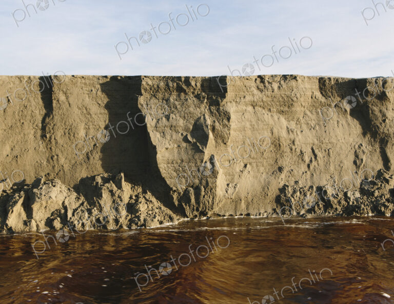 Eroding sand cliffs and fast moving water along intertidal area.