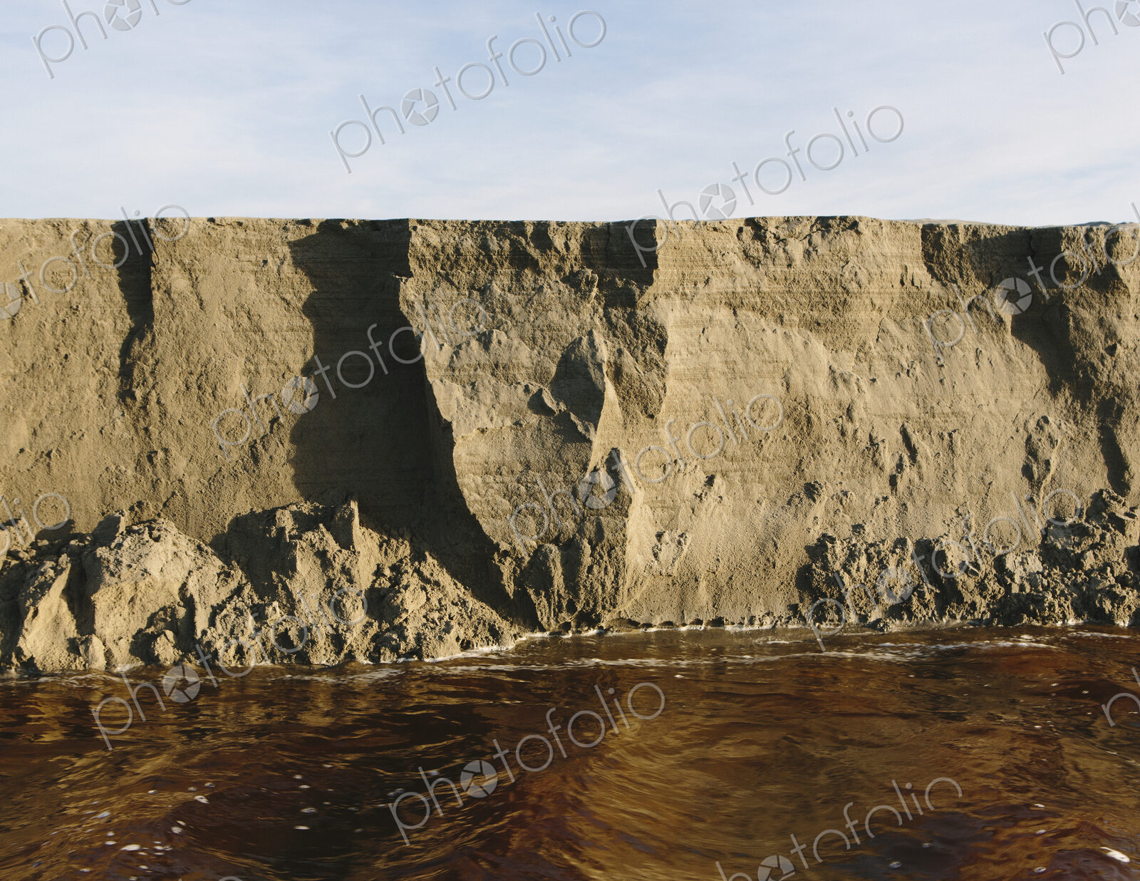 Eroding sand cliffs and fast moving water along intertidal area.
